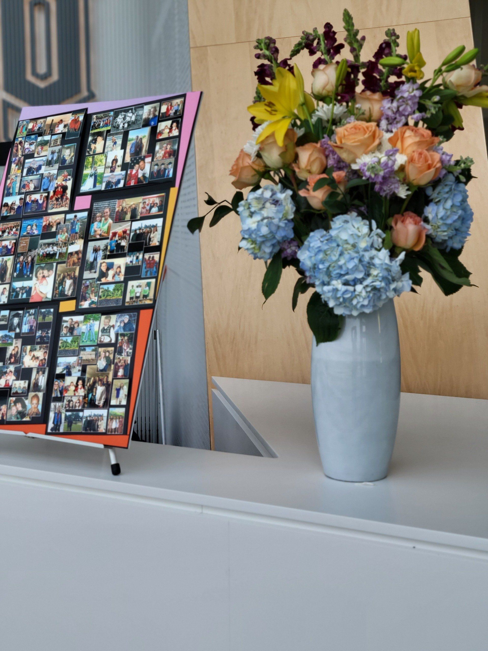 Photo display with framed photos next to a vase of flowers on a white surface.