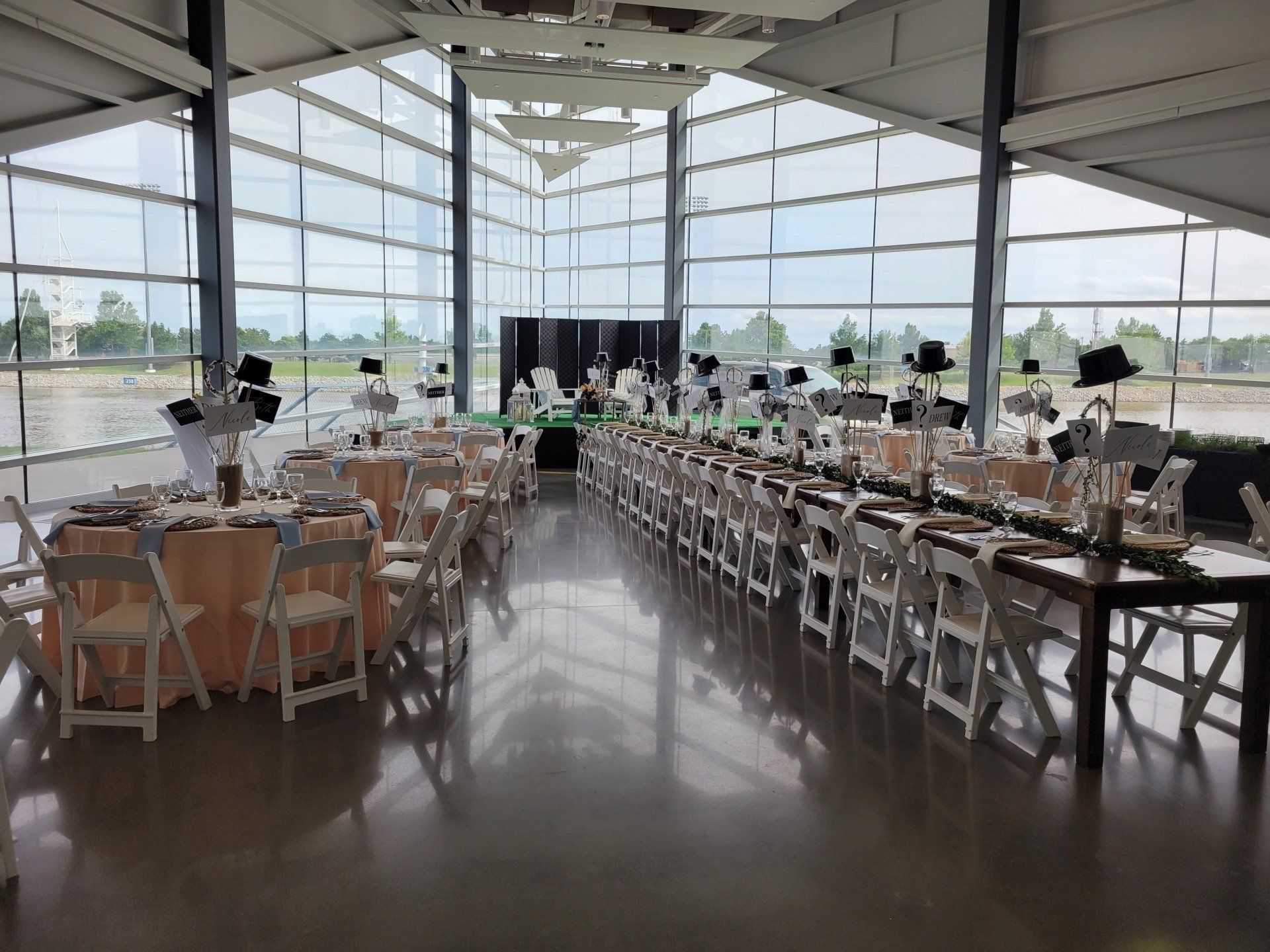 Wedding reception setup in a modern venue with tables, chairs, and decorations; large windows.