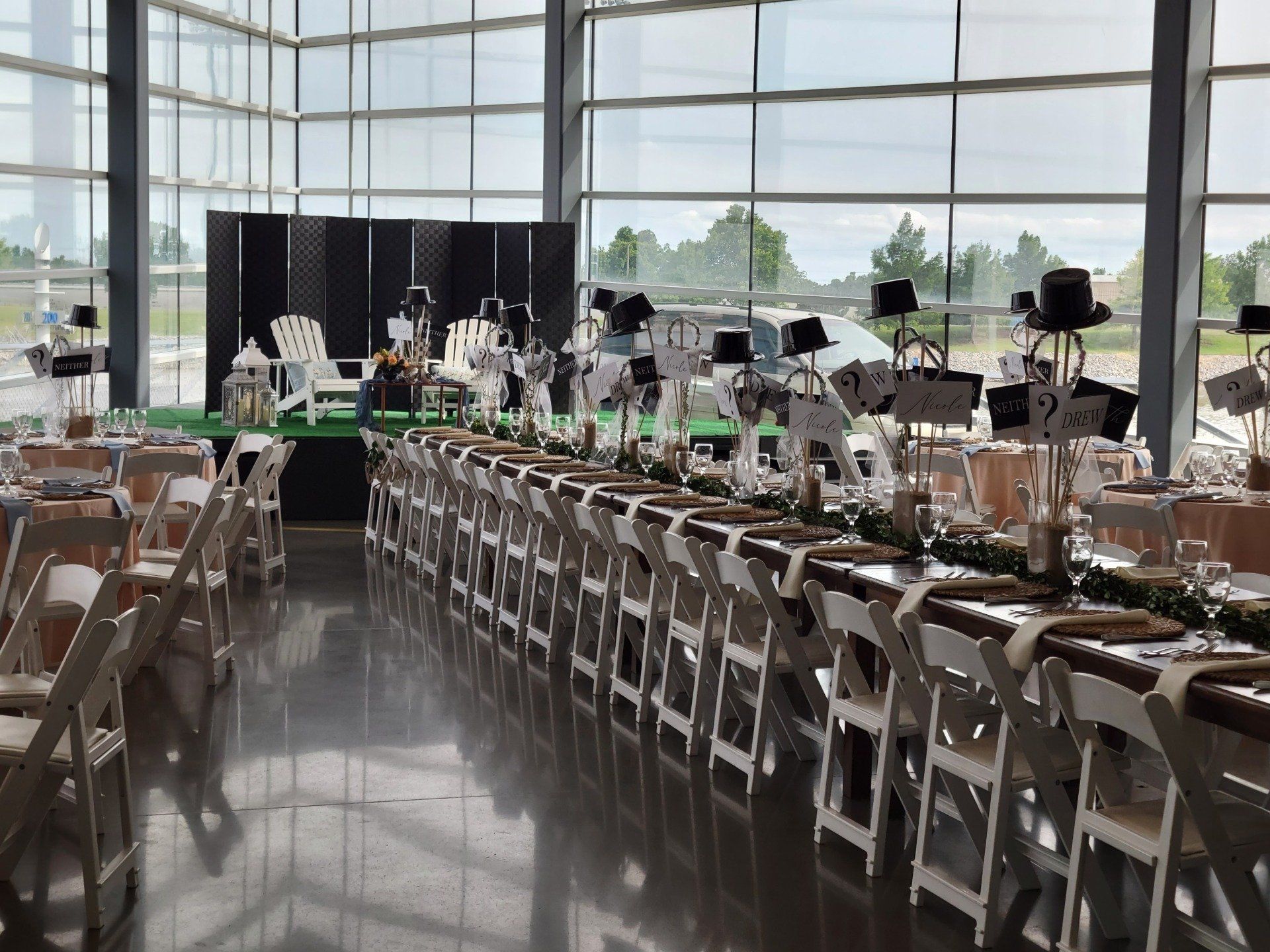Wedding reception setup in a modern building with long tables, white chairs, and decorations.