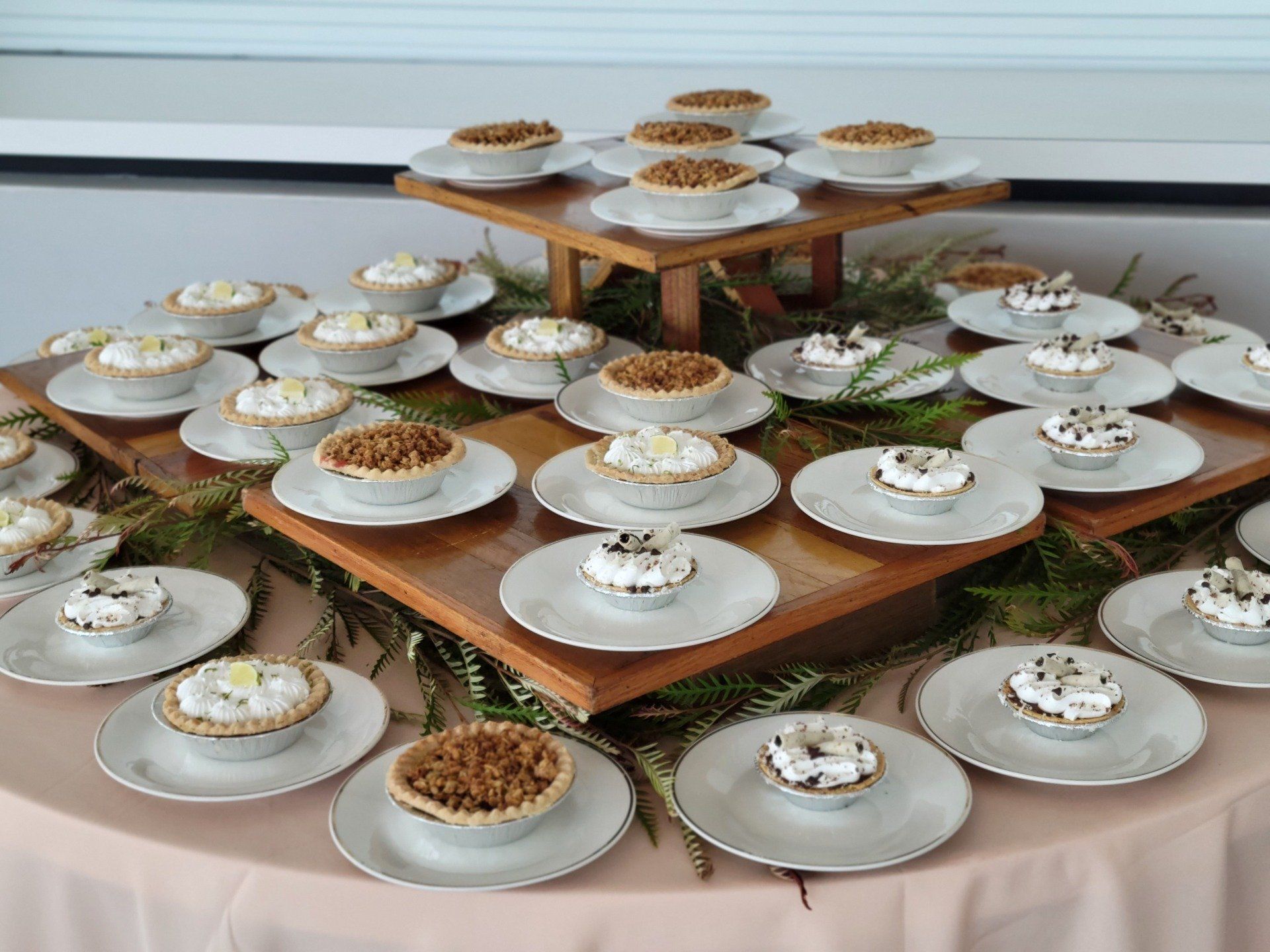 Mini pies on white plates, arranged on tiered wooden platters and a pink tablecloth.