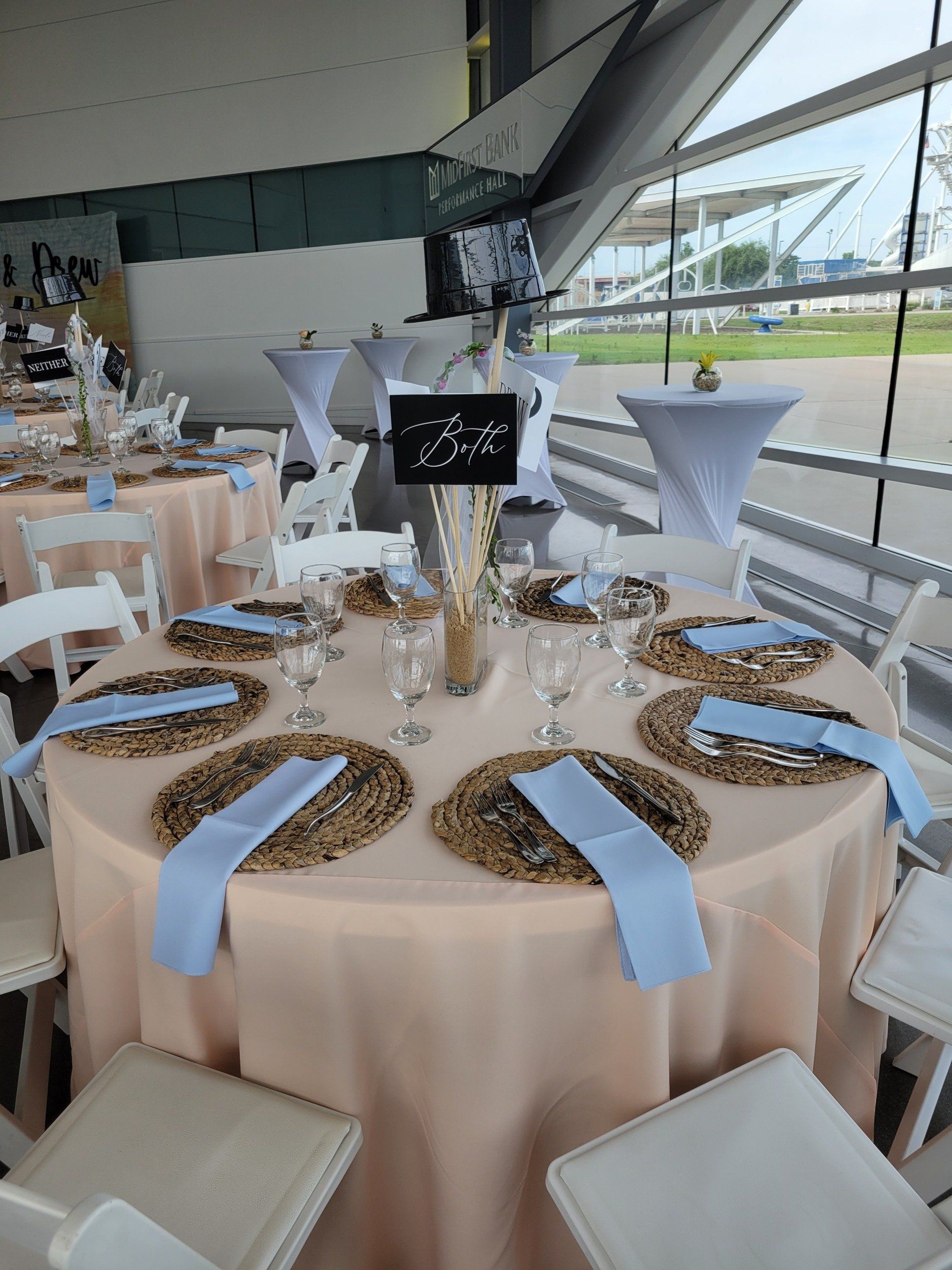 Round table set for a formal event with peach tablecloth, blue napkins, and white chairs.