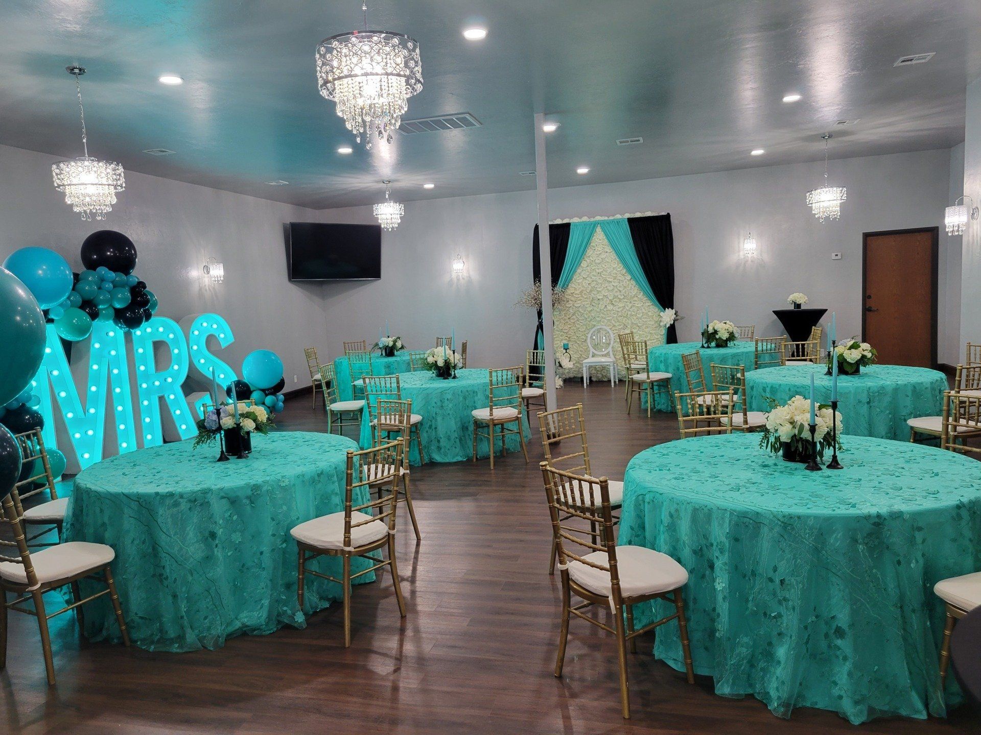 A decorated event space with teal round tables, gold chairs, and