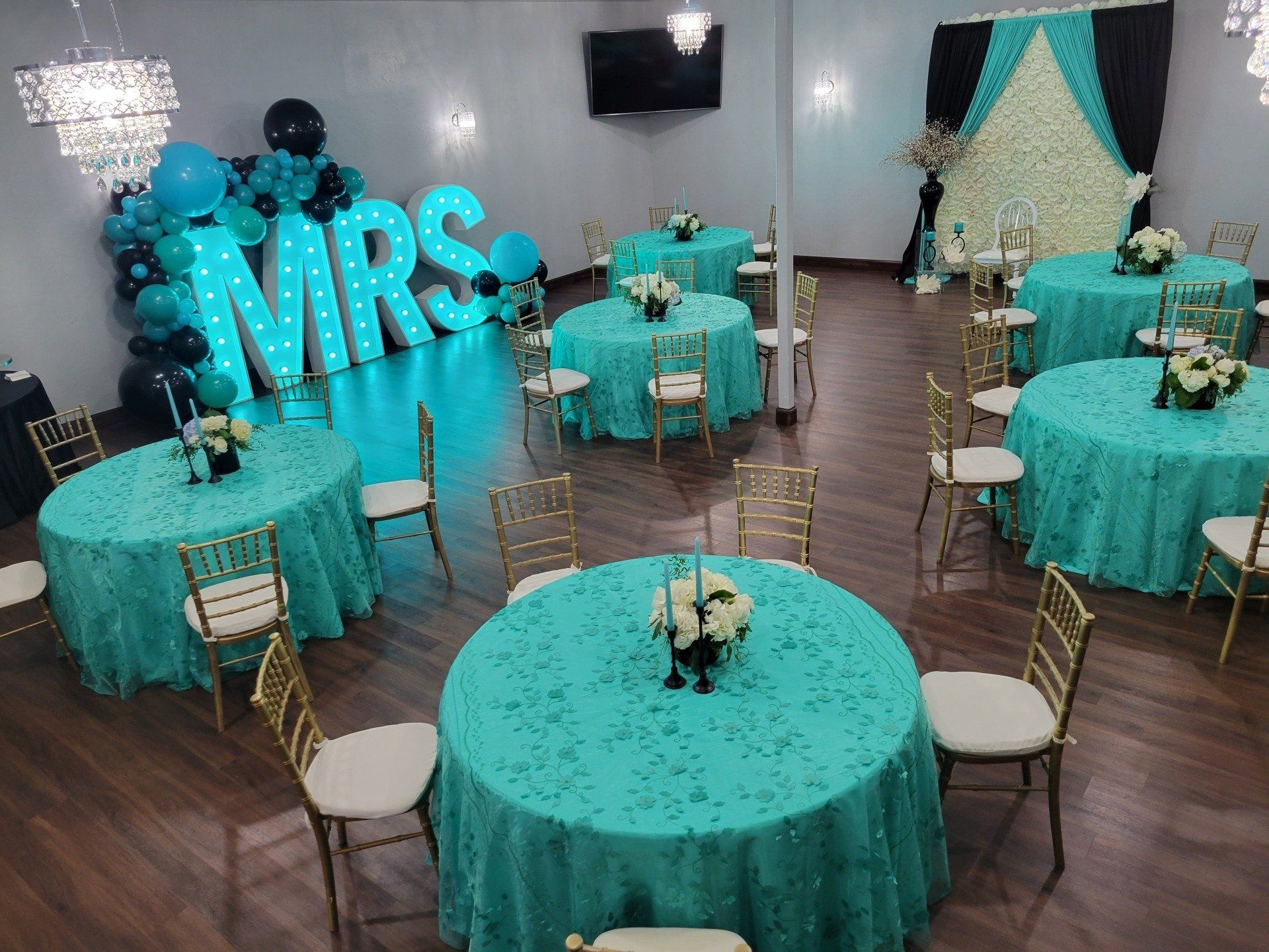 Event space with round tables covered in teal tablecloths, gold chairs, and