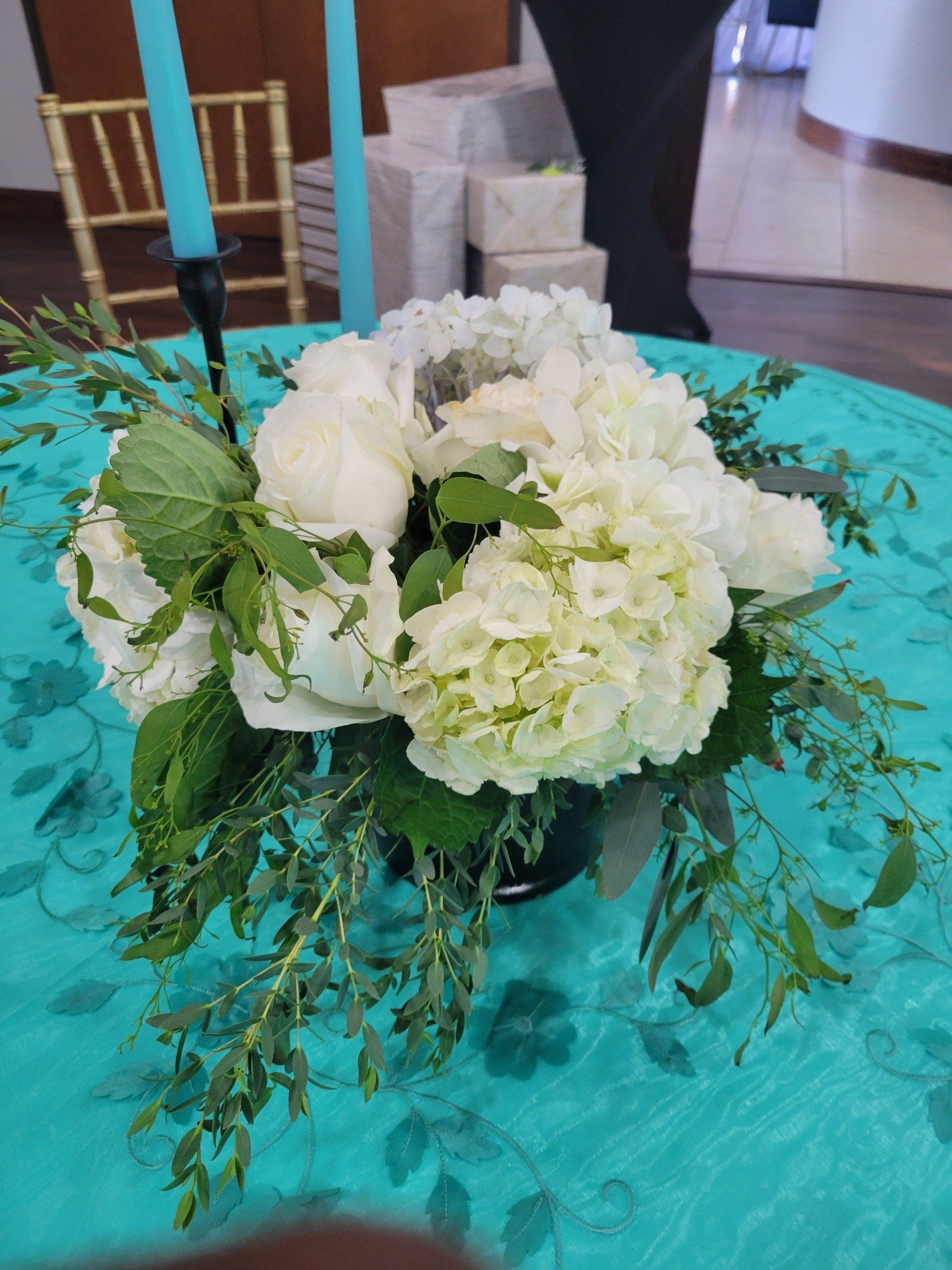 Floral arrangement with white hydrangeas, green leaves, on turquoise cloth.
