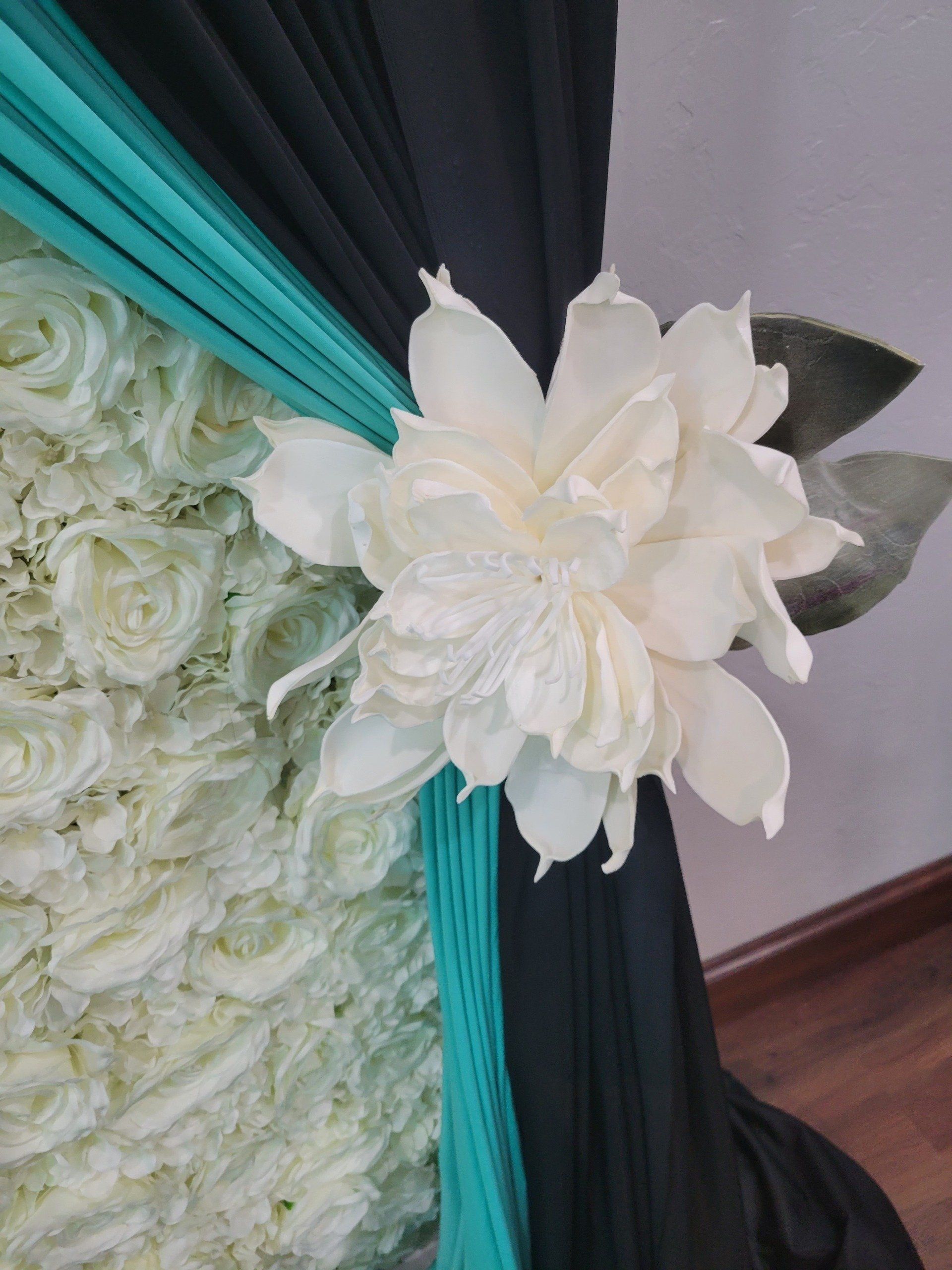 White floral arrangement with black and teal drapery backdrop.