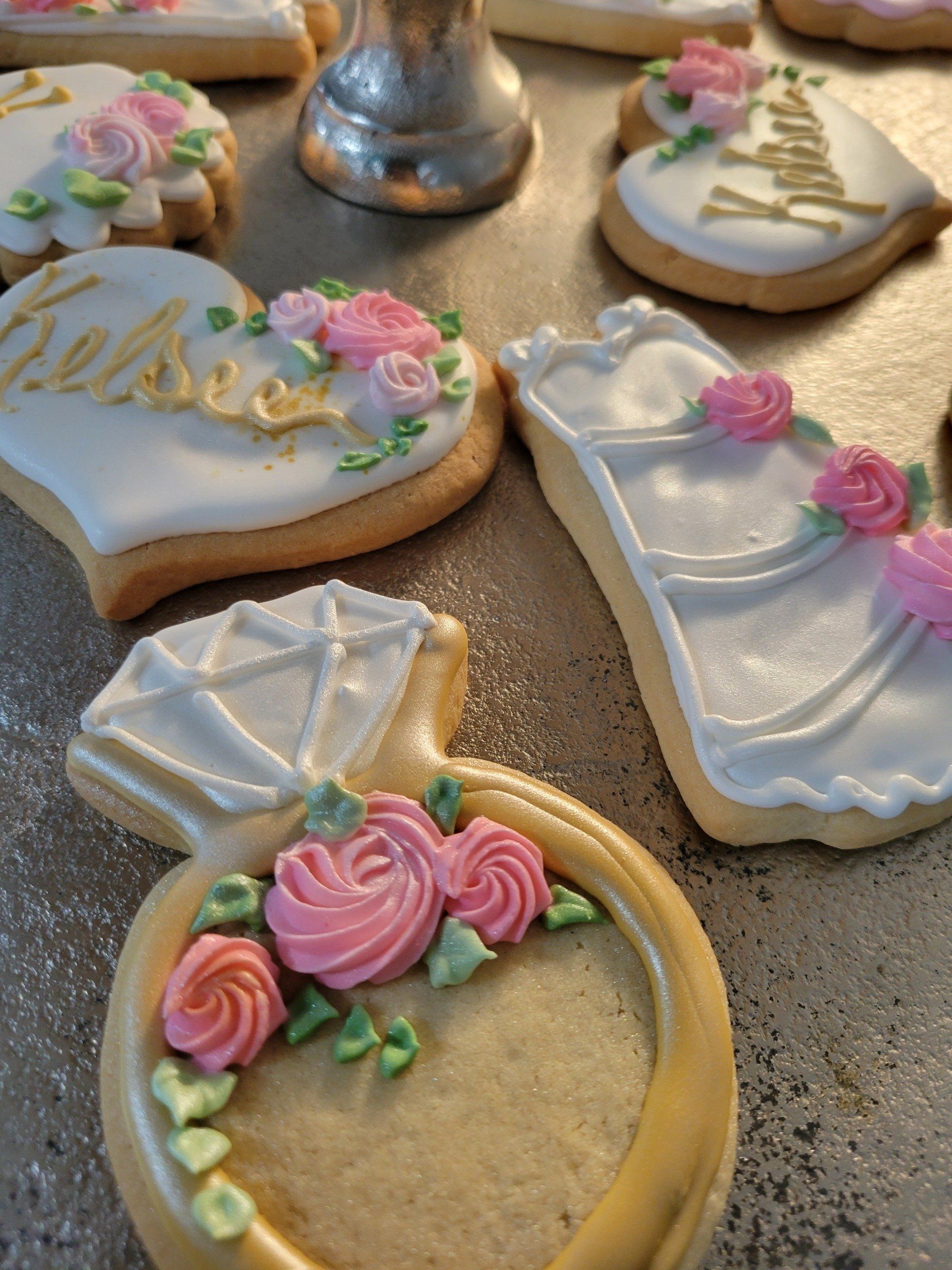 Wedding-themed sugar cookies with white icing, gold details, and pink floral decorations.