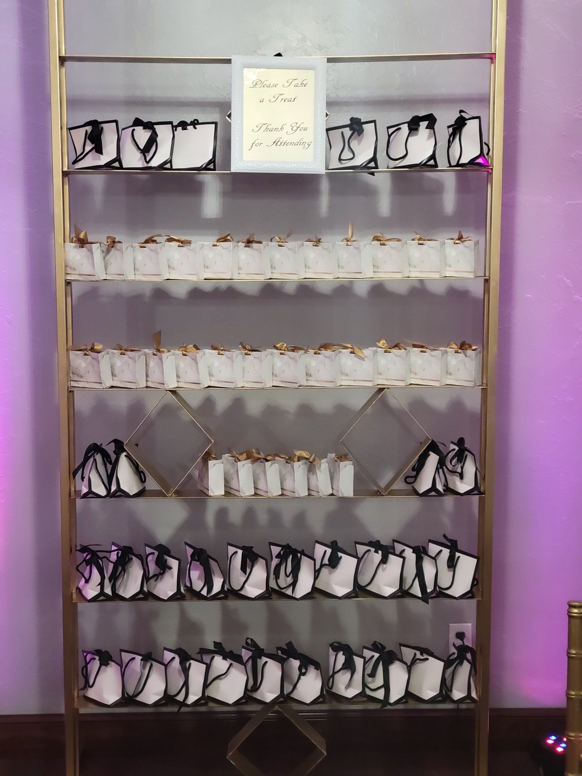 A golden shelf displays white gift bags with black accents and gold trim, many in neat rows.