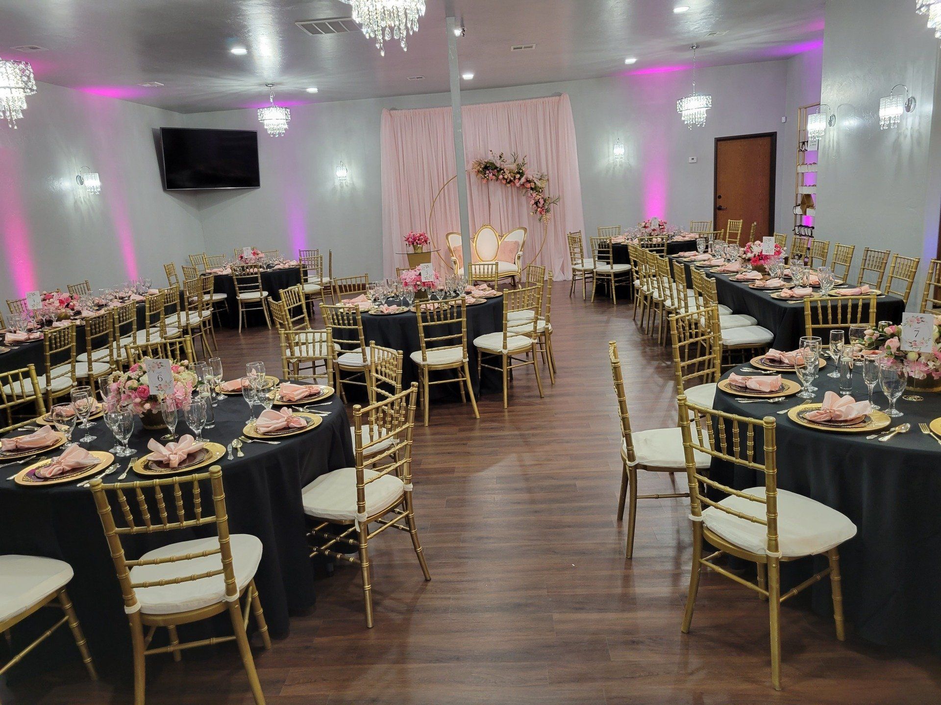 Banquet hall with black tablecloths, gold chairs, and pink decorations, set for an event.