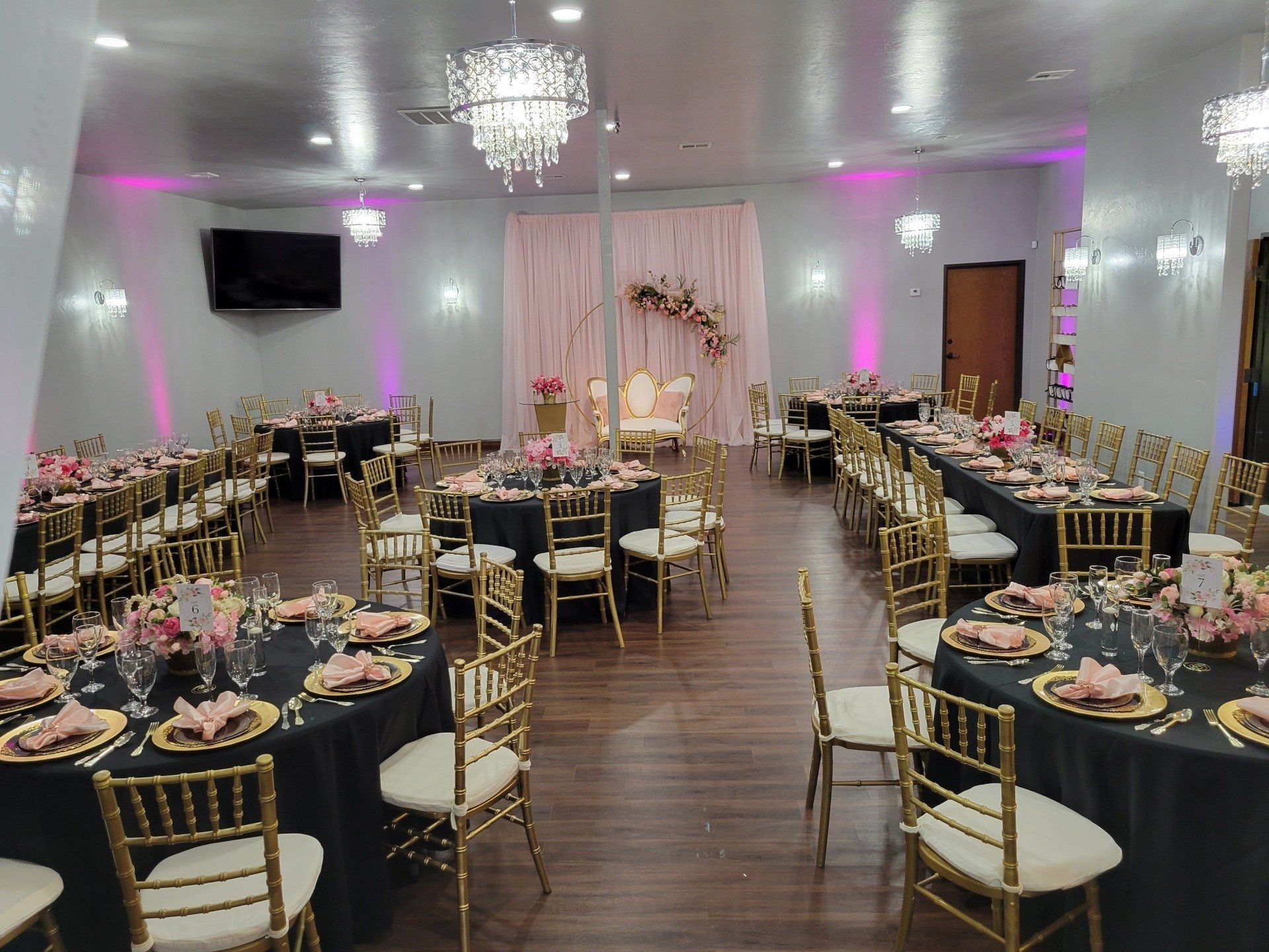 Event space with gold chairs, black tablecloths, and pink floral centerpieces.
