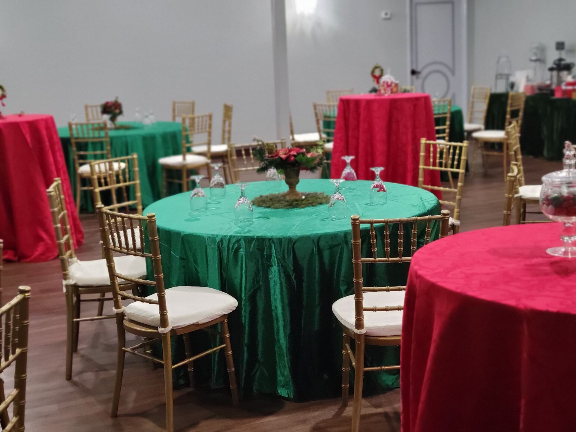 Tables set with red and green tablecloths, gold chairs, and centerpieces in an event space.