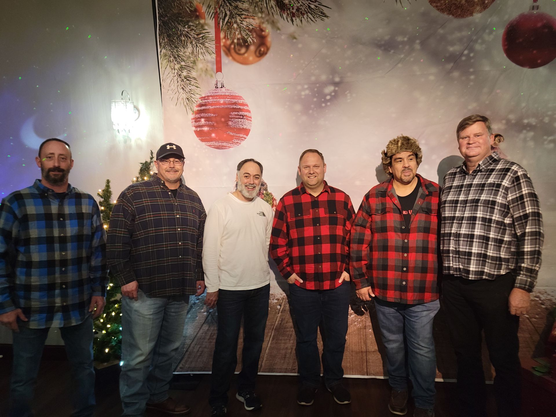 Six men in casual clothing pose in front of a Christmas backdrop.