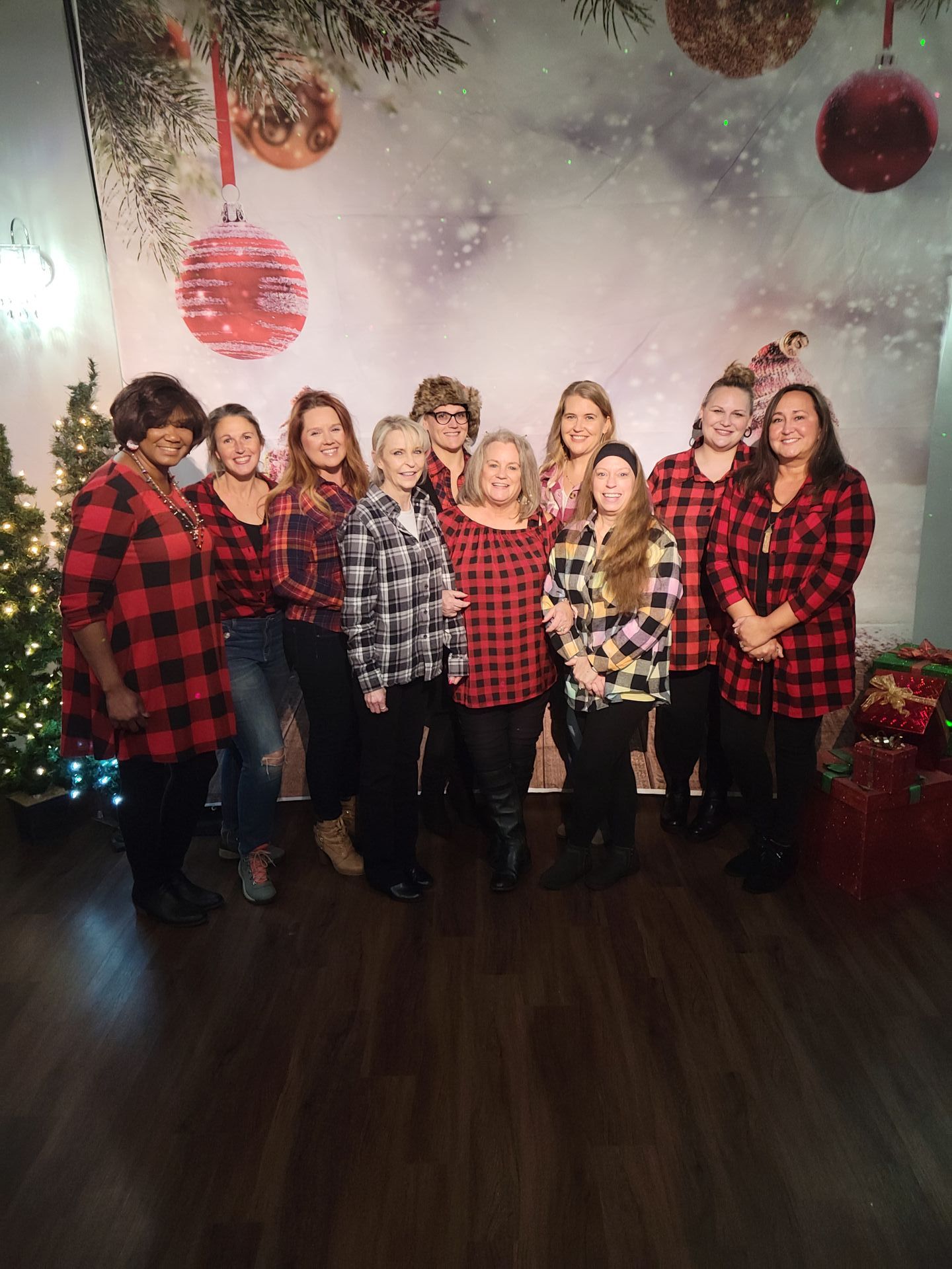 Group of people in red and black plaid shirts posing in front of a holiday backdrop.