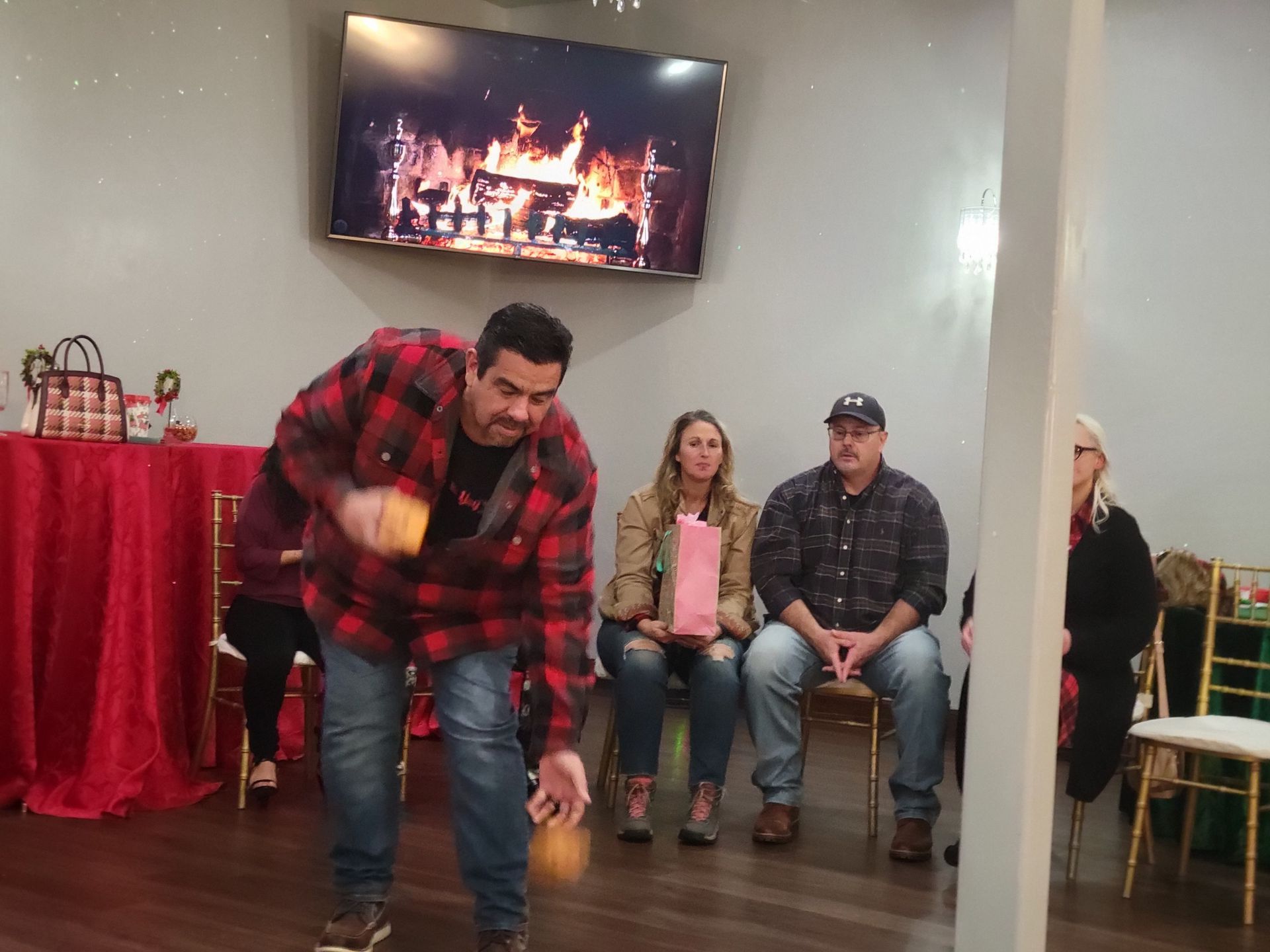 Man throwing a bean bag at a game in a party setting; three people watch.