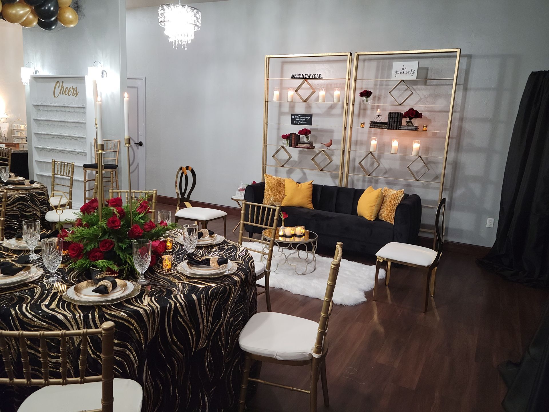 Elegant event space, decorated in black and gold. Tables set, seating area with sofa and shelves.