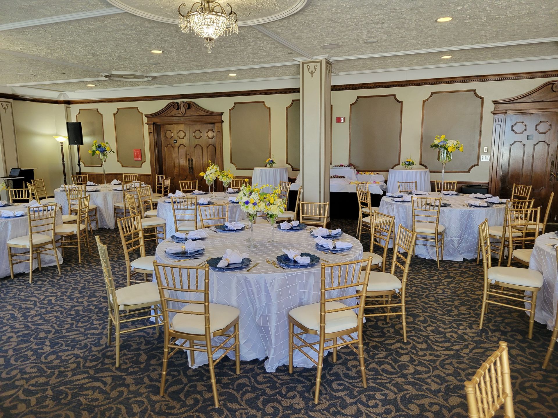 Banquet hall set for event with round tables, gold chairs, and floral centerpieces.