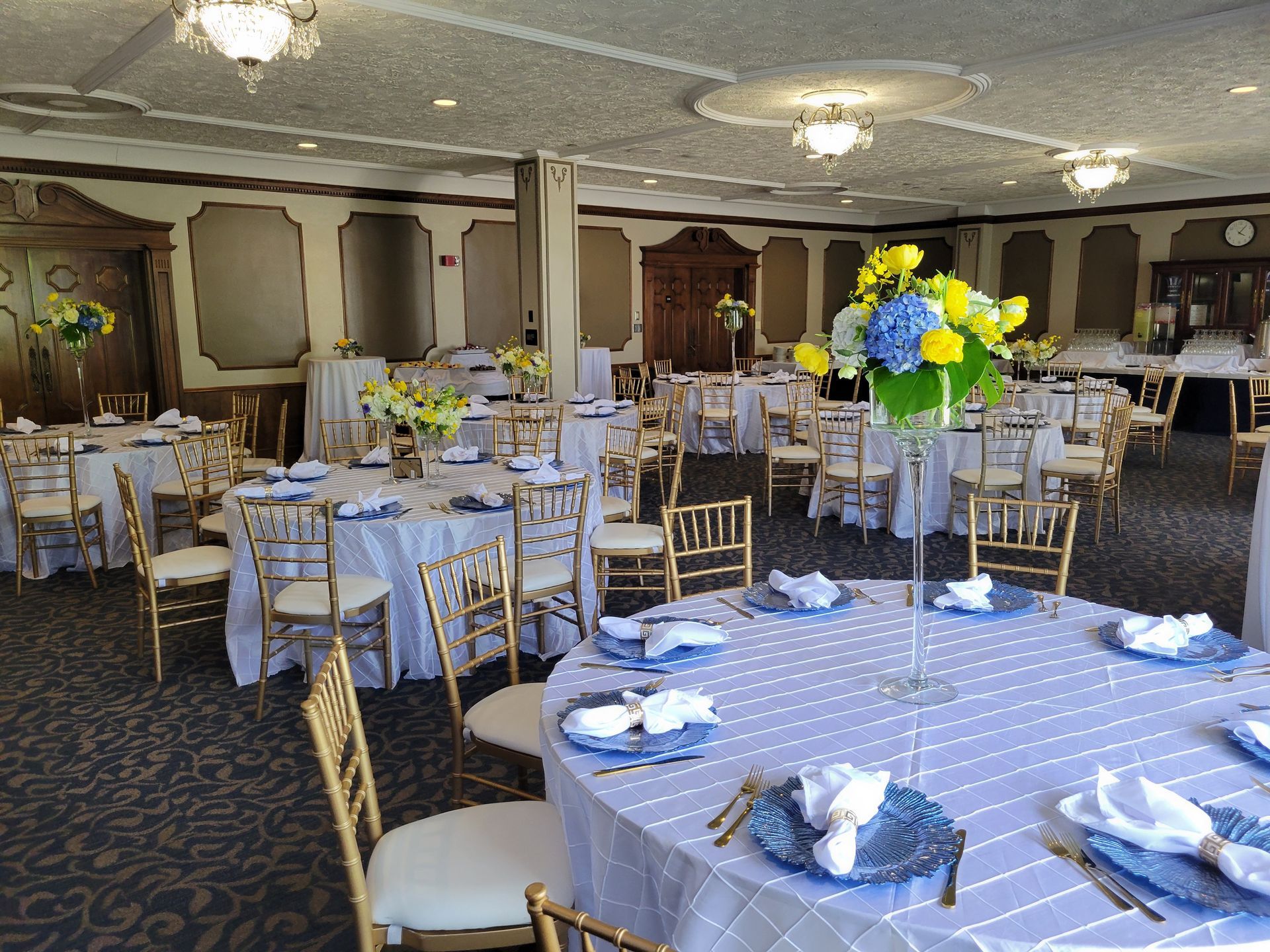 Elegant event space with round tables set with blue and white decor, gold chairs, and floral centerpieces.