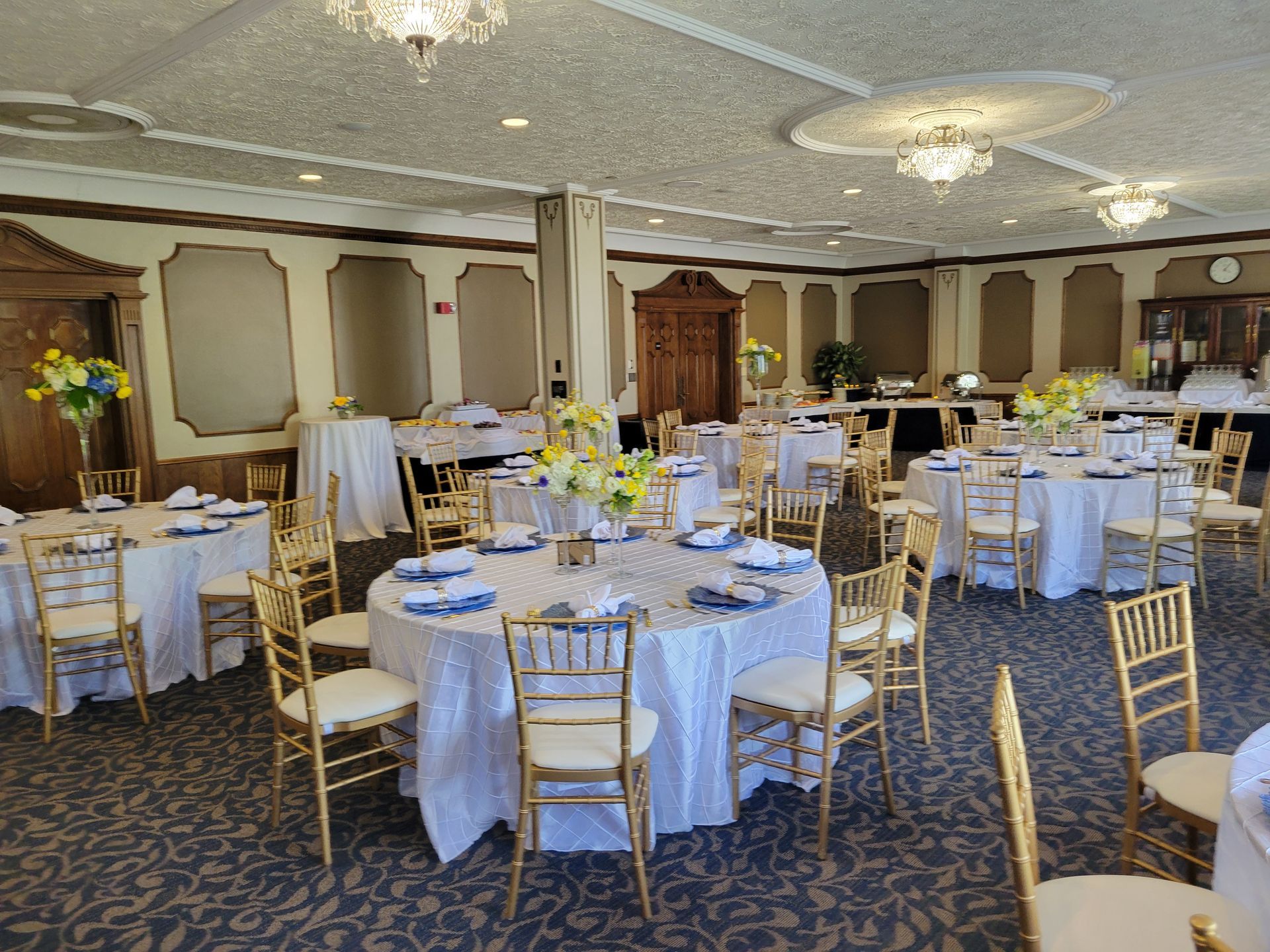Elegant banquet room with round tables, white linens, gold chairs, and floral centerpieces.