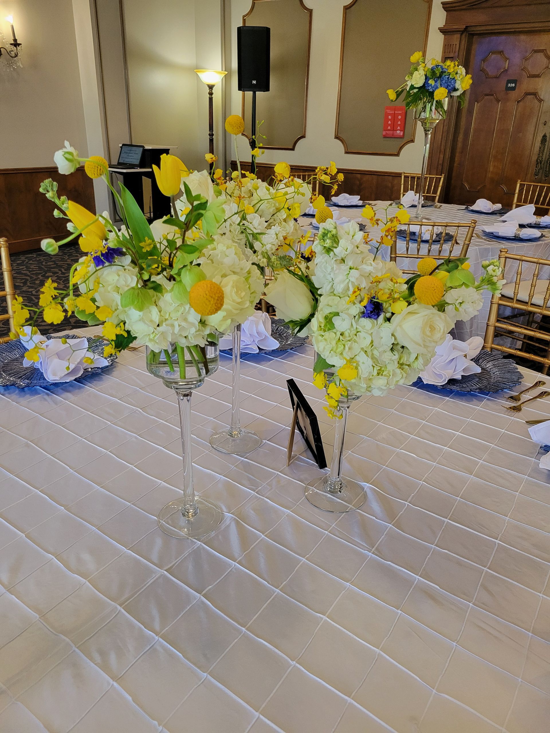 Centerpieces with white and yellow flowers on a table set for an event.