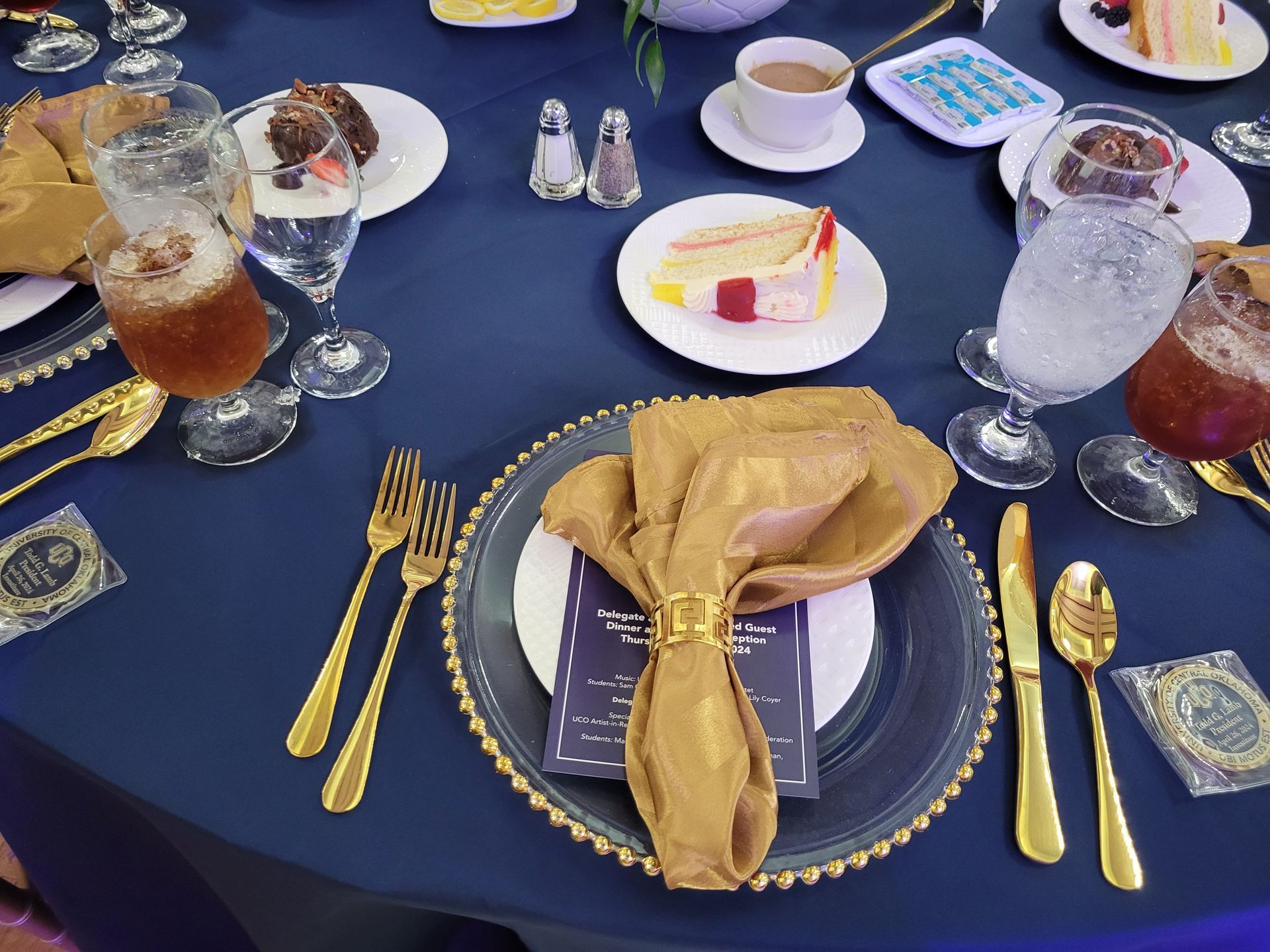 Formal table setting with gold utensils, navy blue tablecloth, and plates with food and drinks.