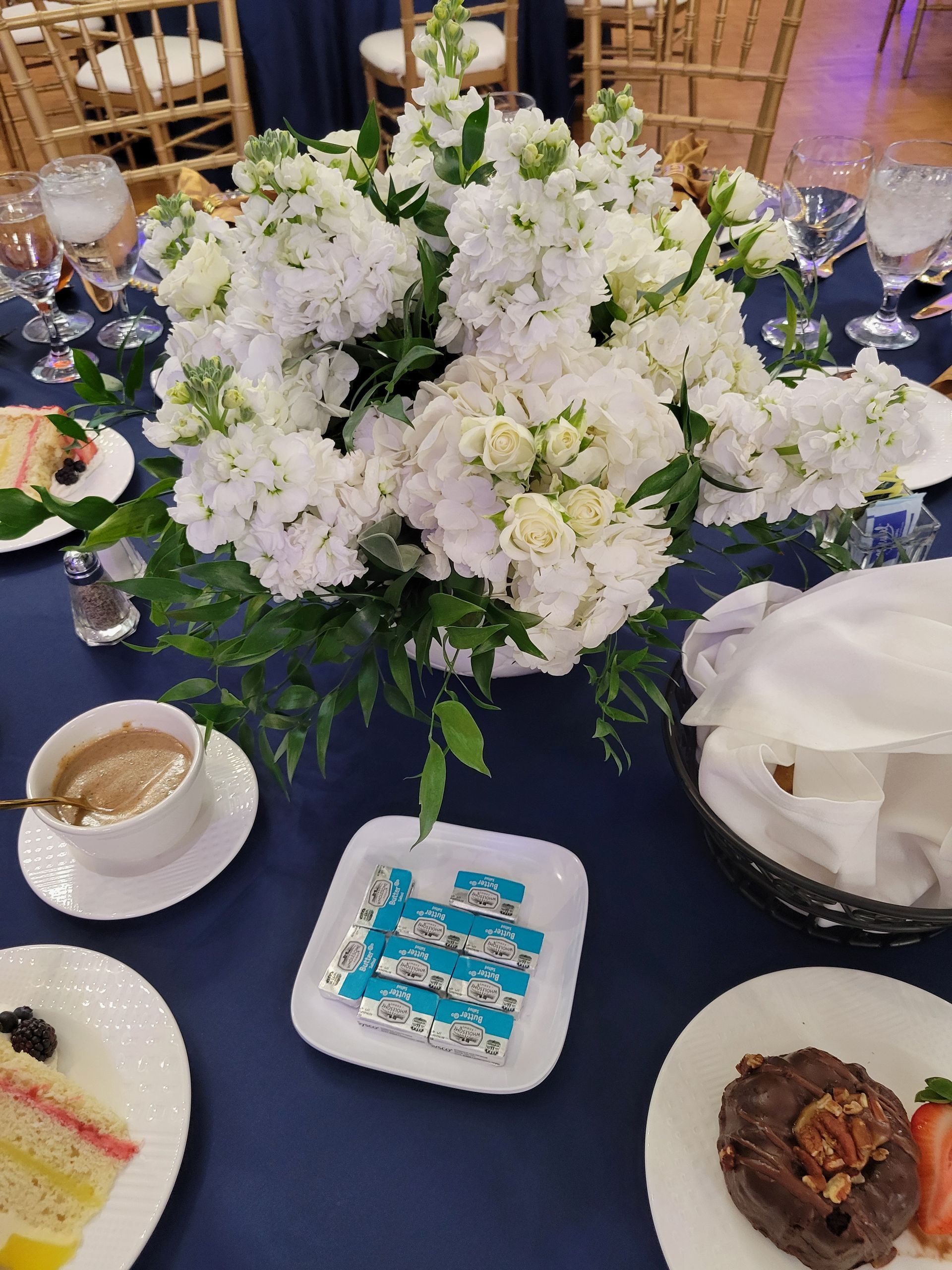 Table setting with white floral arrangement, dessert plates, coffee cup, and navy tablecloth.