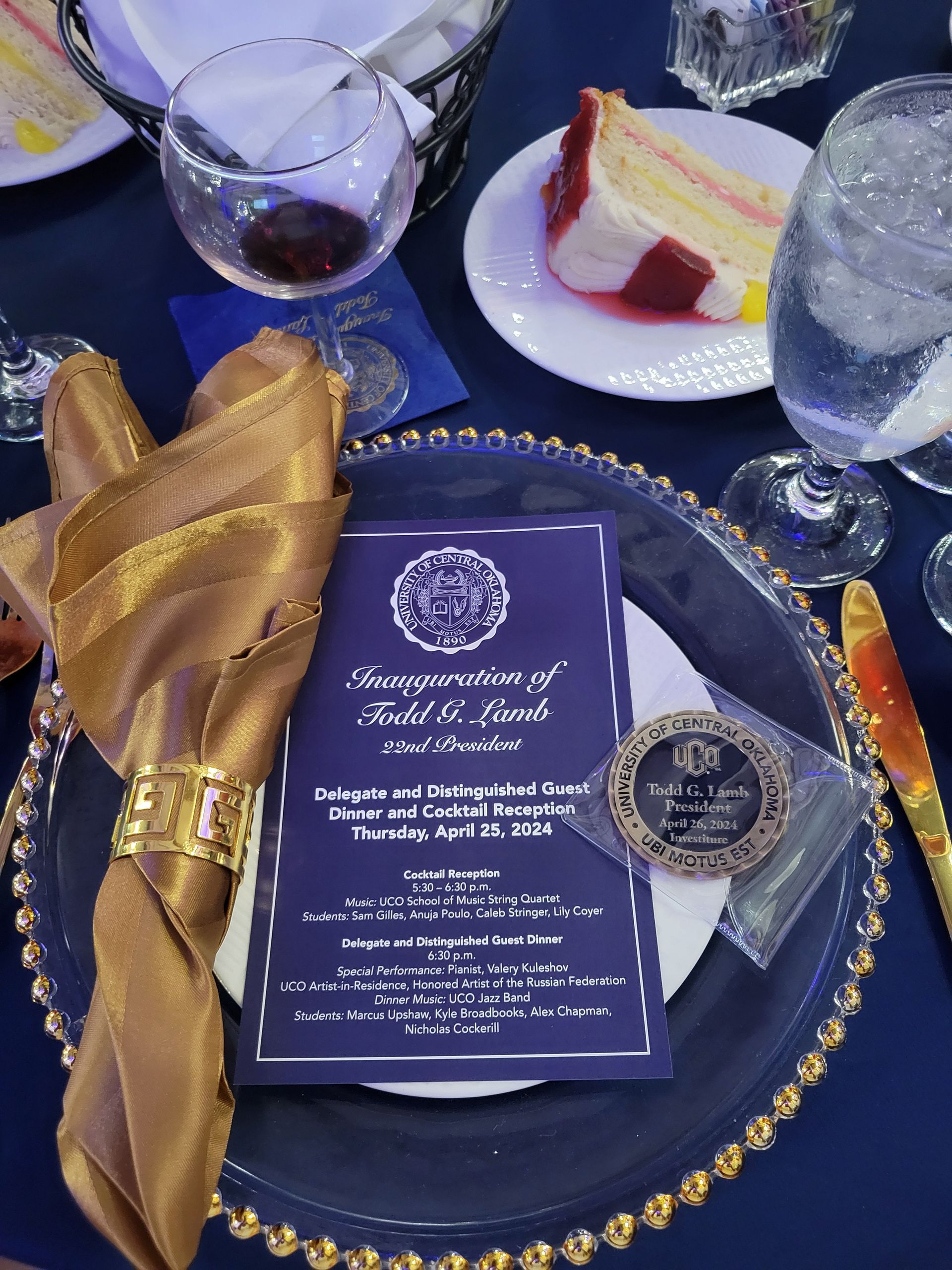 Table setting with gold napkin, invitation, dessert, and drink at an inauguration ceremony.
