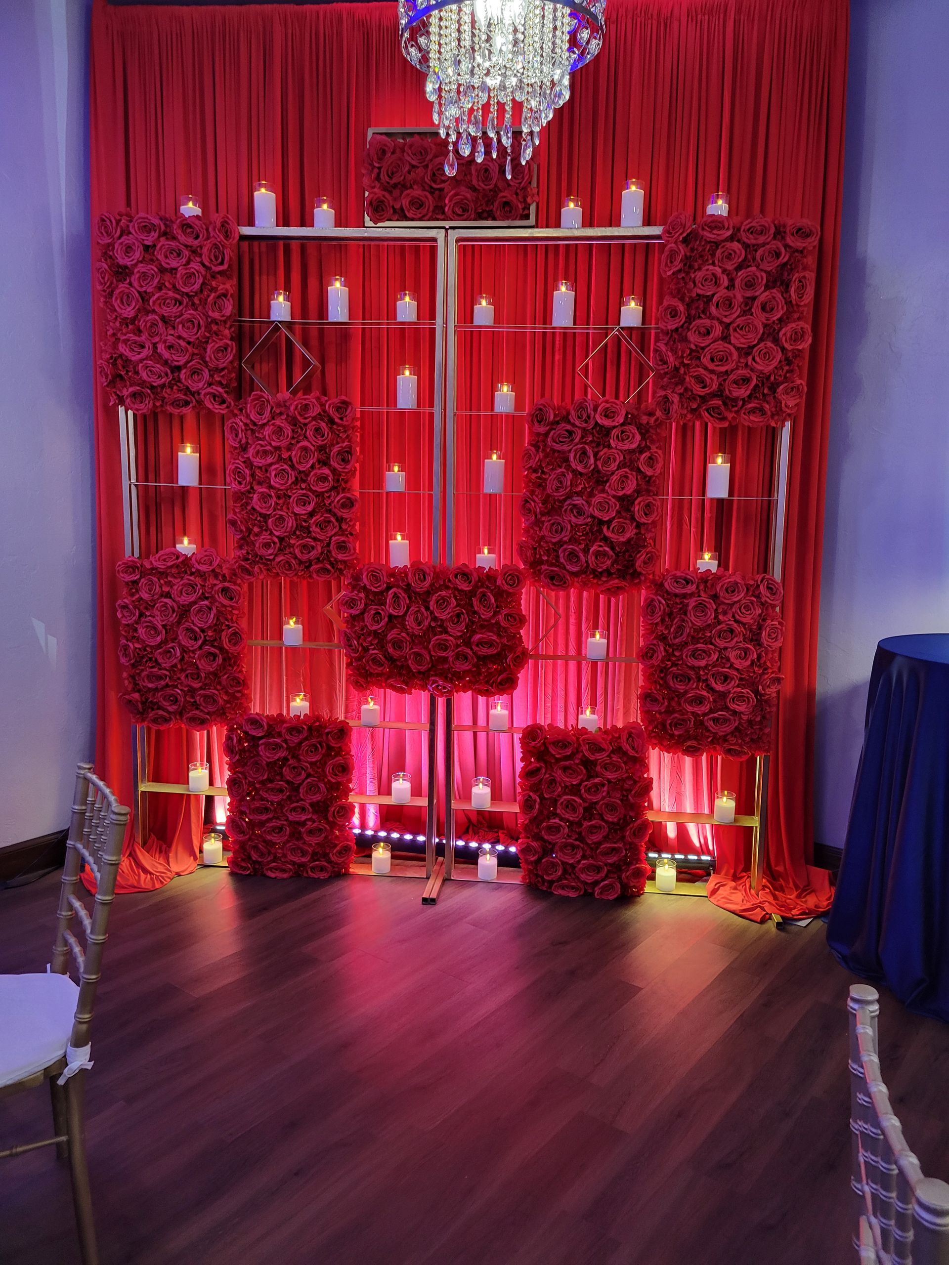 Red rose wall with candles, gold frame, red curtain backdrop, and chandelier.