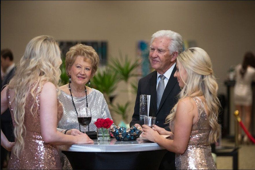 People socializing at a formal event, gathered around a small table, holding drinks.