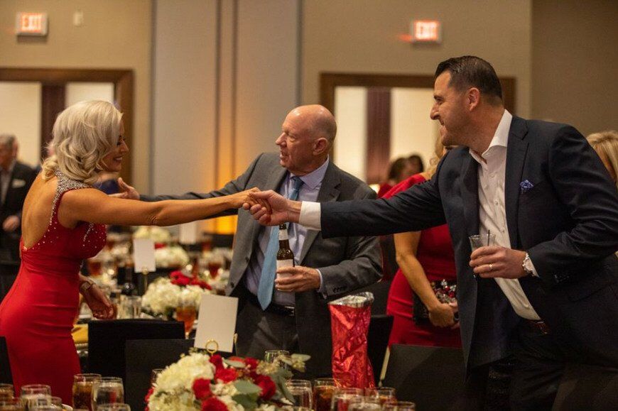 Woman in red dress shakes hands with man in blue suit at event.