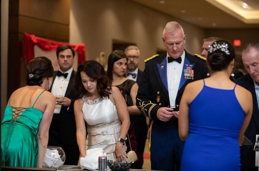 People at an event checking in, one in military uniform. Various formal dresses, drinks, and a raffle.
