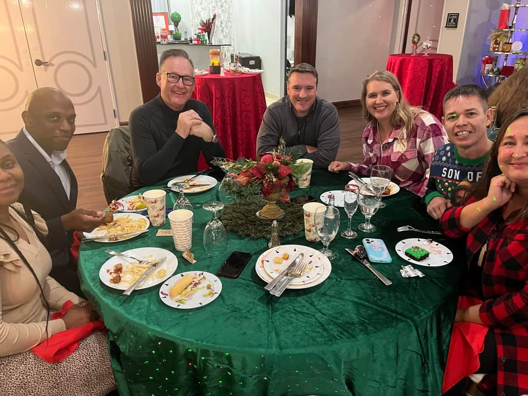 People seated at a round table with food and decorations, smiling.