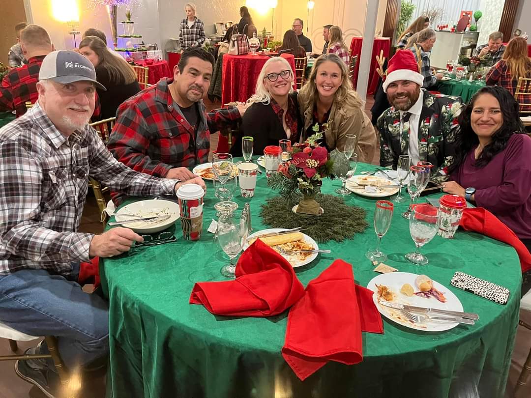 People at a Christmas party seated around a green table with red napkins and decorations.