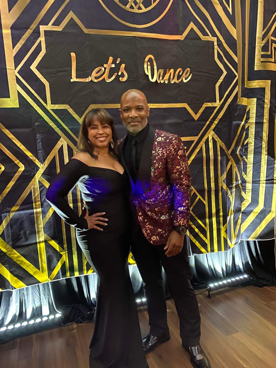 Couple in formal attire pose in front of a “Let’s Dance” backdrop.