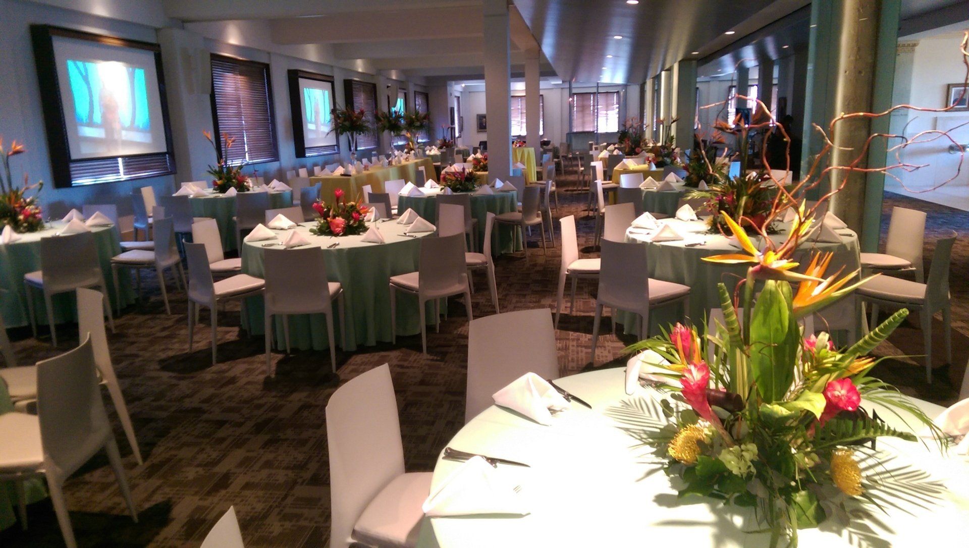 Event room with round tables draped in light green, white chairs, floral centerpieces.
