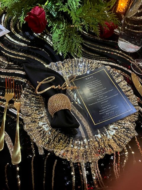 Elegant table setting with black napkin, gold charger, menu, and gold flatware.