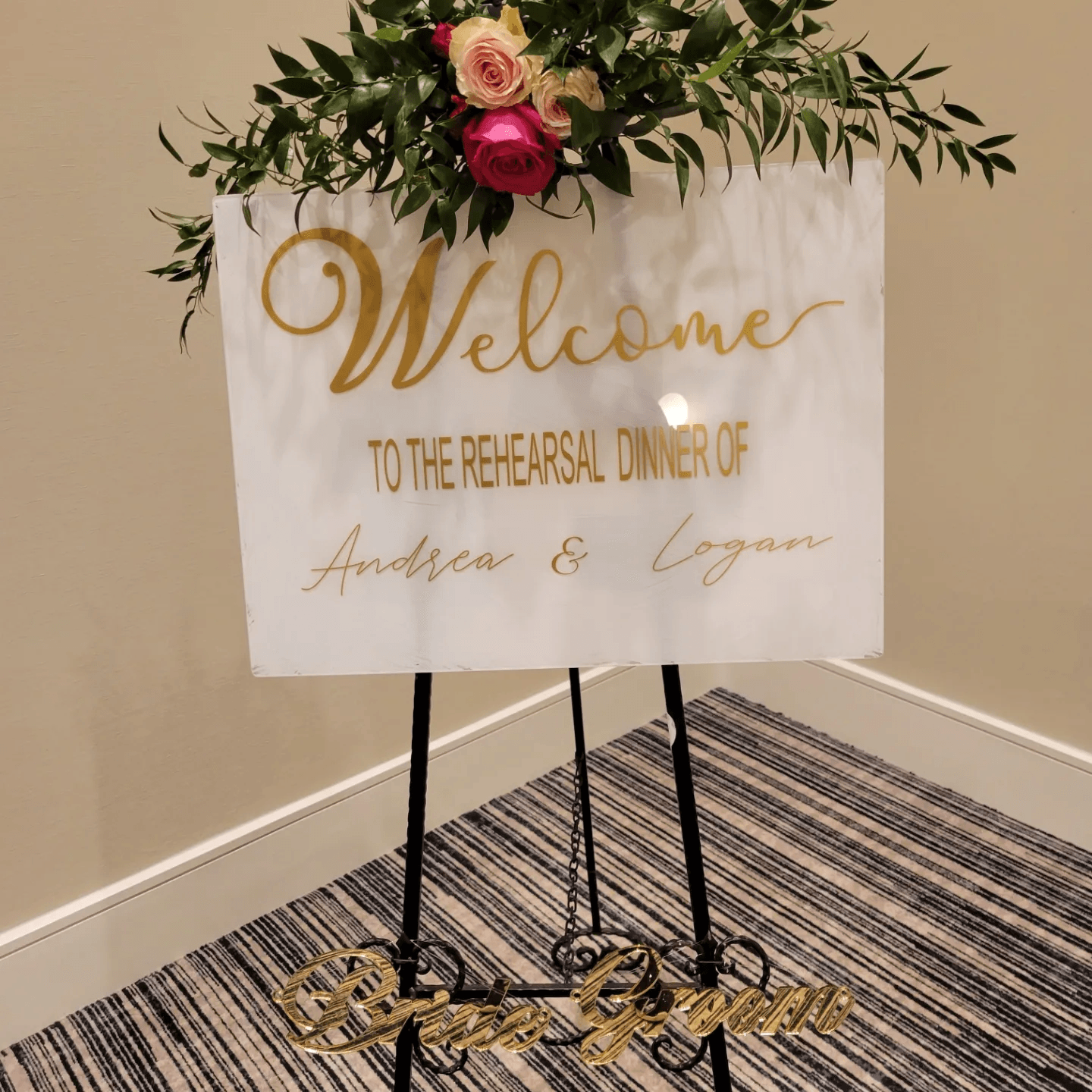 Welcome sign for Andrea & Logan's rehearsal dinner with floral arrangement on an easel.