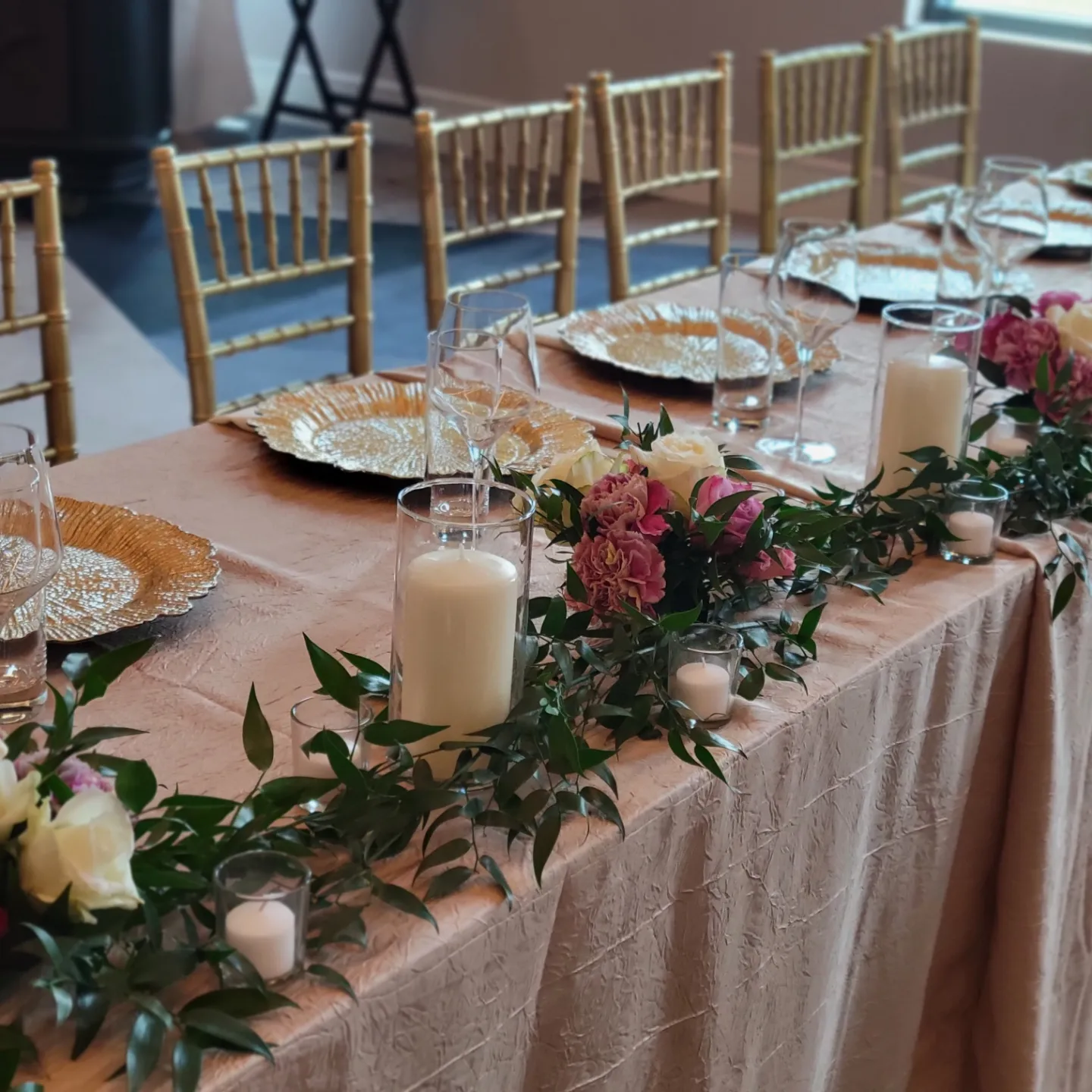 Formal dining table set with gold chairs, plates, and floral garland.