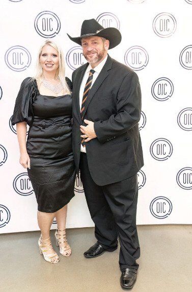 A man in a cowboy hat and a woman in a black dress pose for a photo at an event with the 