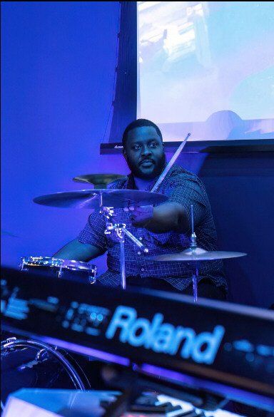Drummer playing a drum set, with blue lighting. 