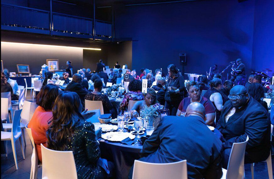 Large room with seated guests at tables, blue lighting.