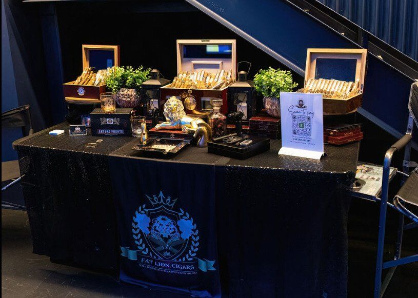 A table displaying cigars, accessories, and promotional materials, likely at a cigar shop, draped with a black tablecloth.