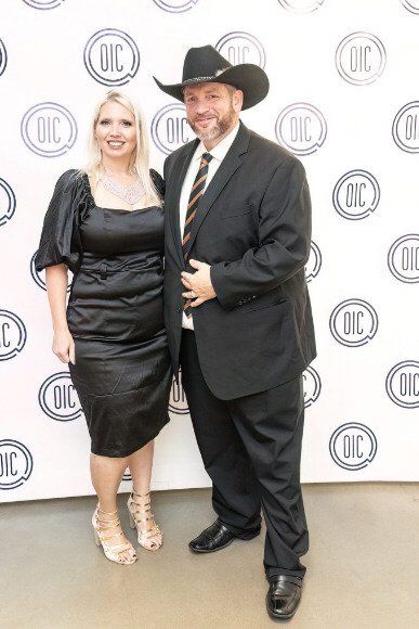 A man in a cowboy hat and suit stands with a woman in a black dress, both smiling at an event.