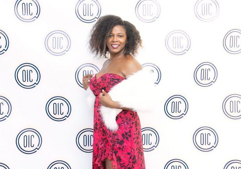 Woman in red dress and white fur wrap posing in front of a backdrop with 