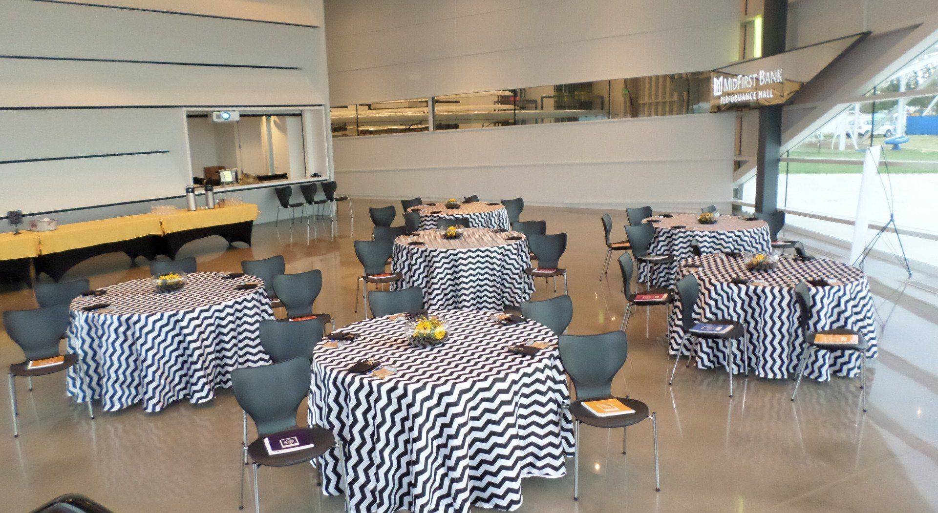 Tables set for an event inside a building. Round tables with black and white zigzag tablecloths and black chairs.