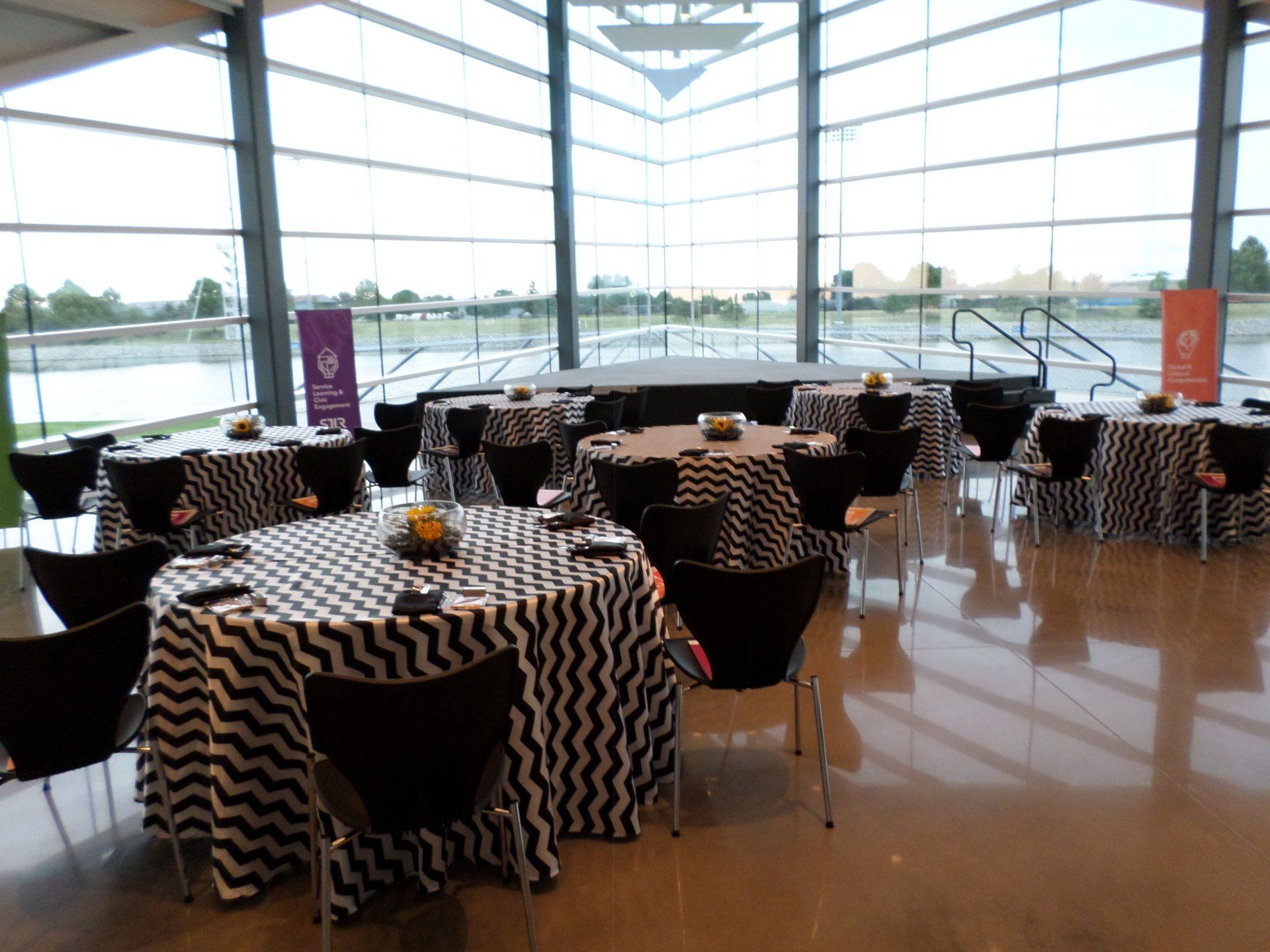 Event room with round tables draped in black and white chevron, black chairs, and large windows.