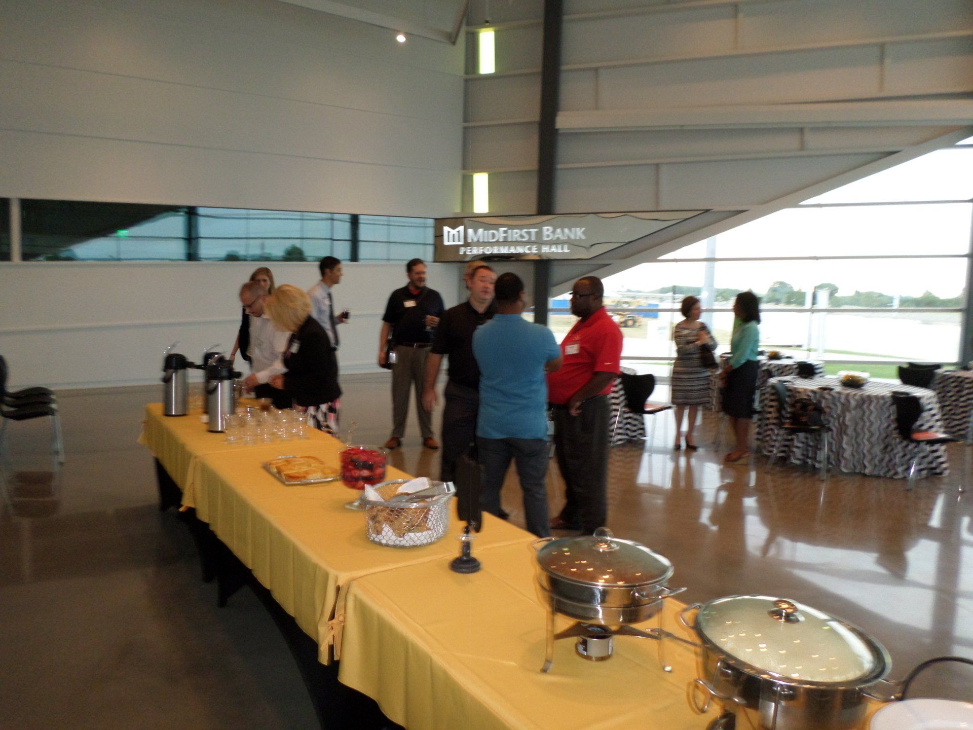 People at a business event with food table; large, open room; window and buffet.