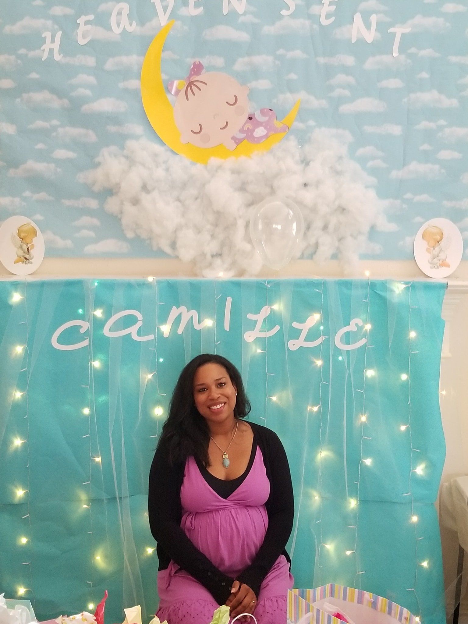 Pregnant woman in pink dress at a baby shower with decorations: clouds, moon, and the name 
