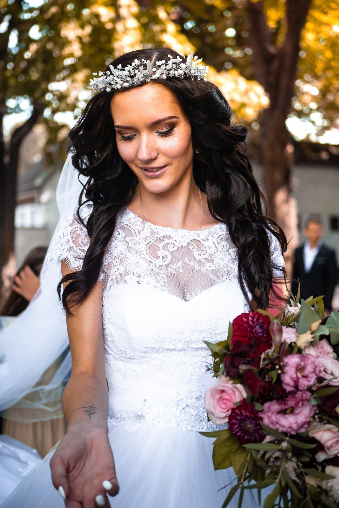 Bride in white lace dress and floral crown holding bouquet, smiling.