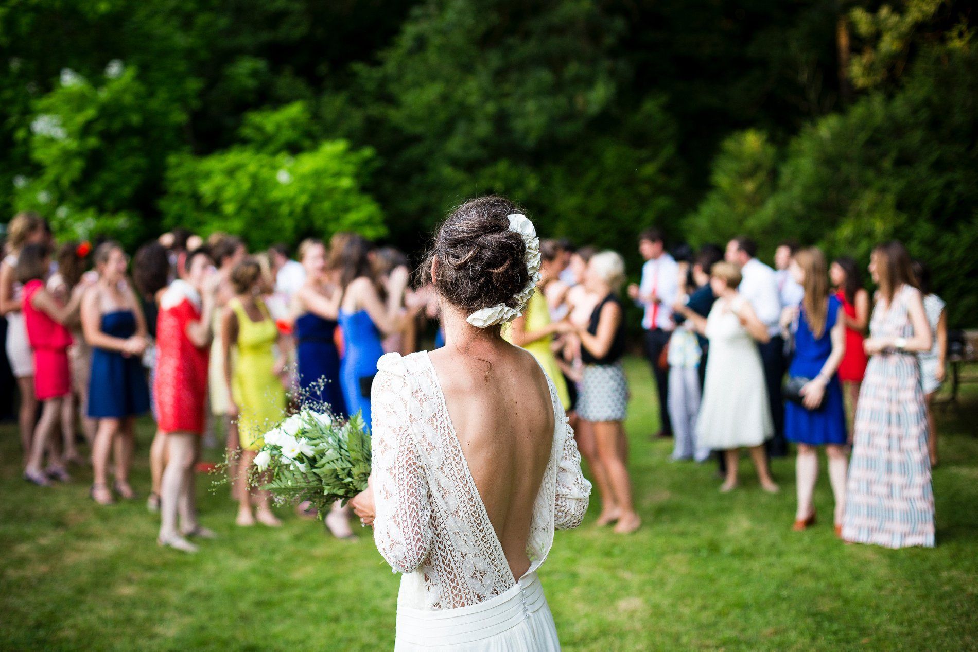 Bride with bouquet faces a crowd of wedding guests in a garden.