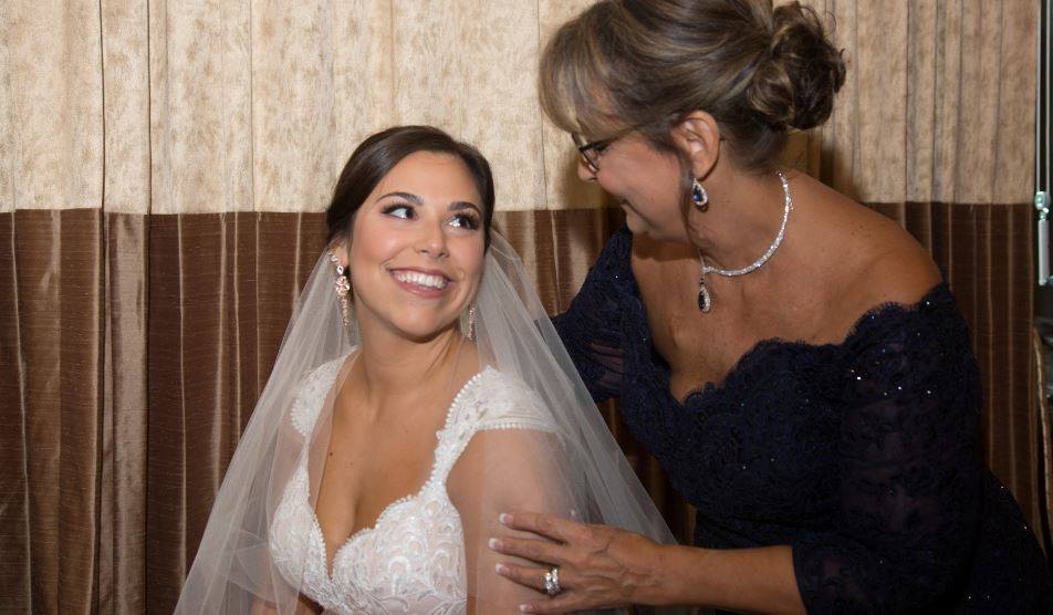 Bride smiles, mother adjusts her dress. Interior with gold wall.