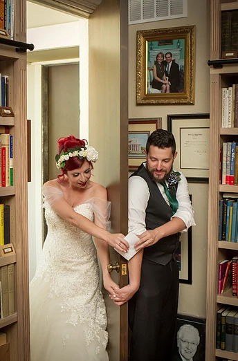 Bride and groom holding hands, standing in a doorway lined with bookshelves, getting ready for the wedding.